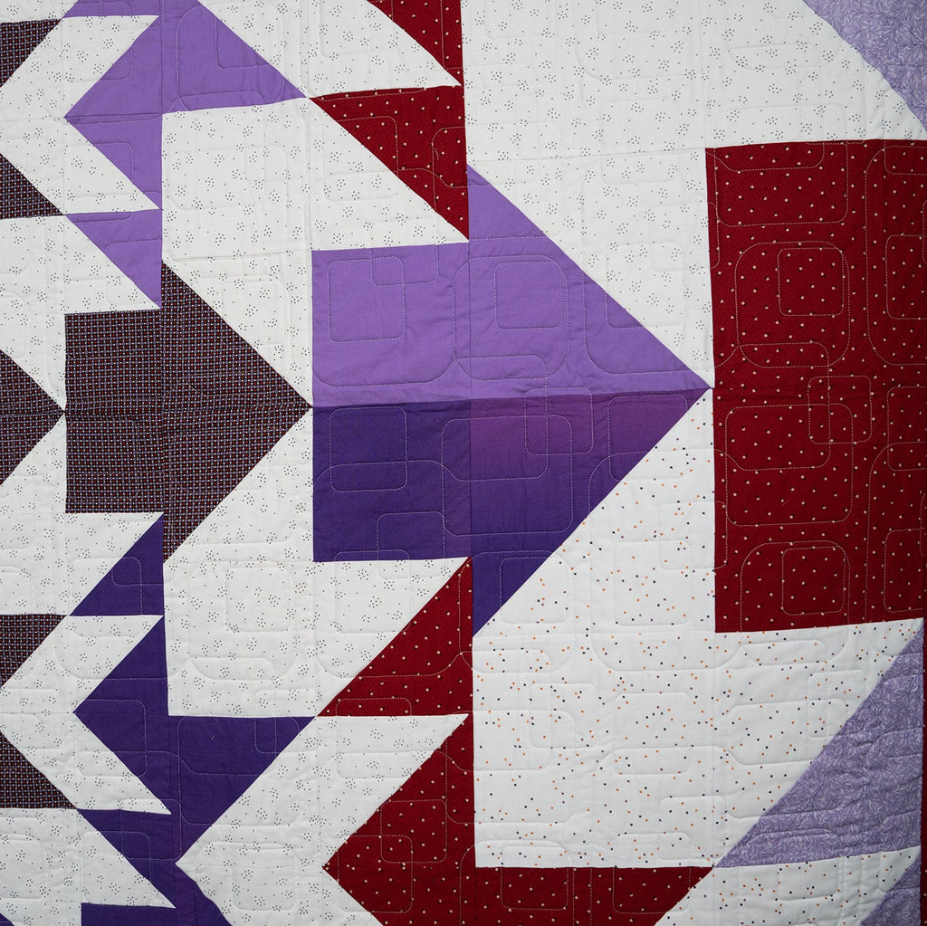 Quilt with geometric pattern in purple, red, and white