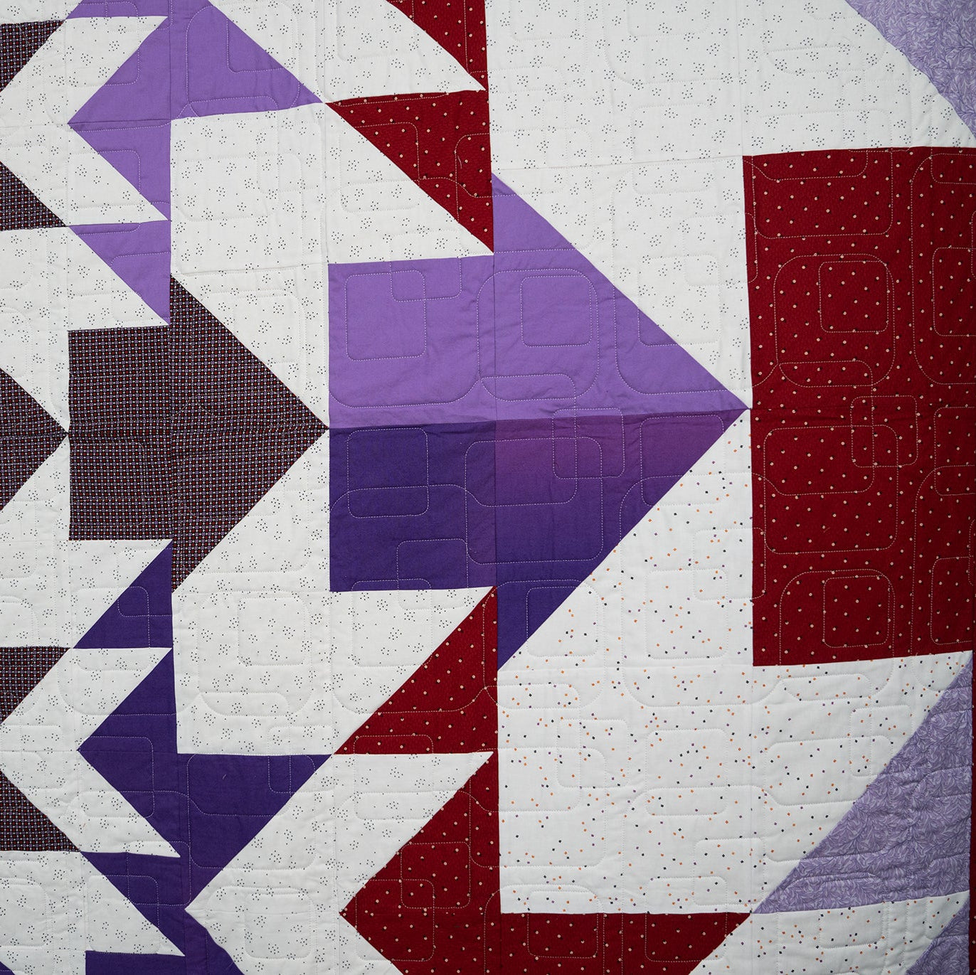Quilt with geometric pattern in purple, red, and white