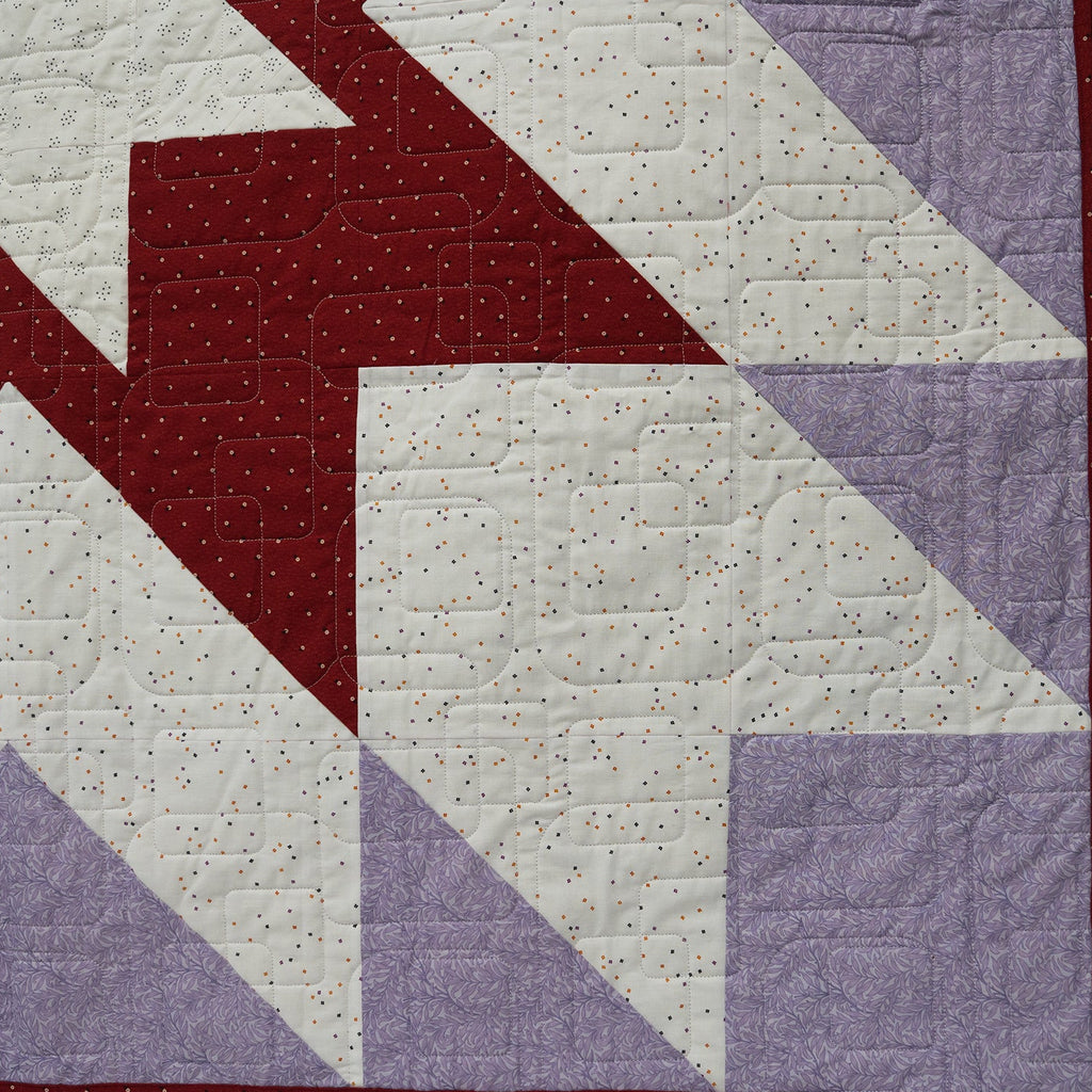 Quilt with geometric pattern featuring red, purple, and white triangles on a white background