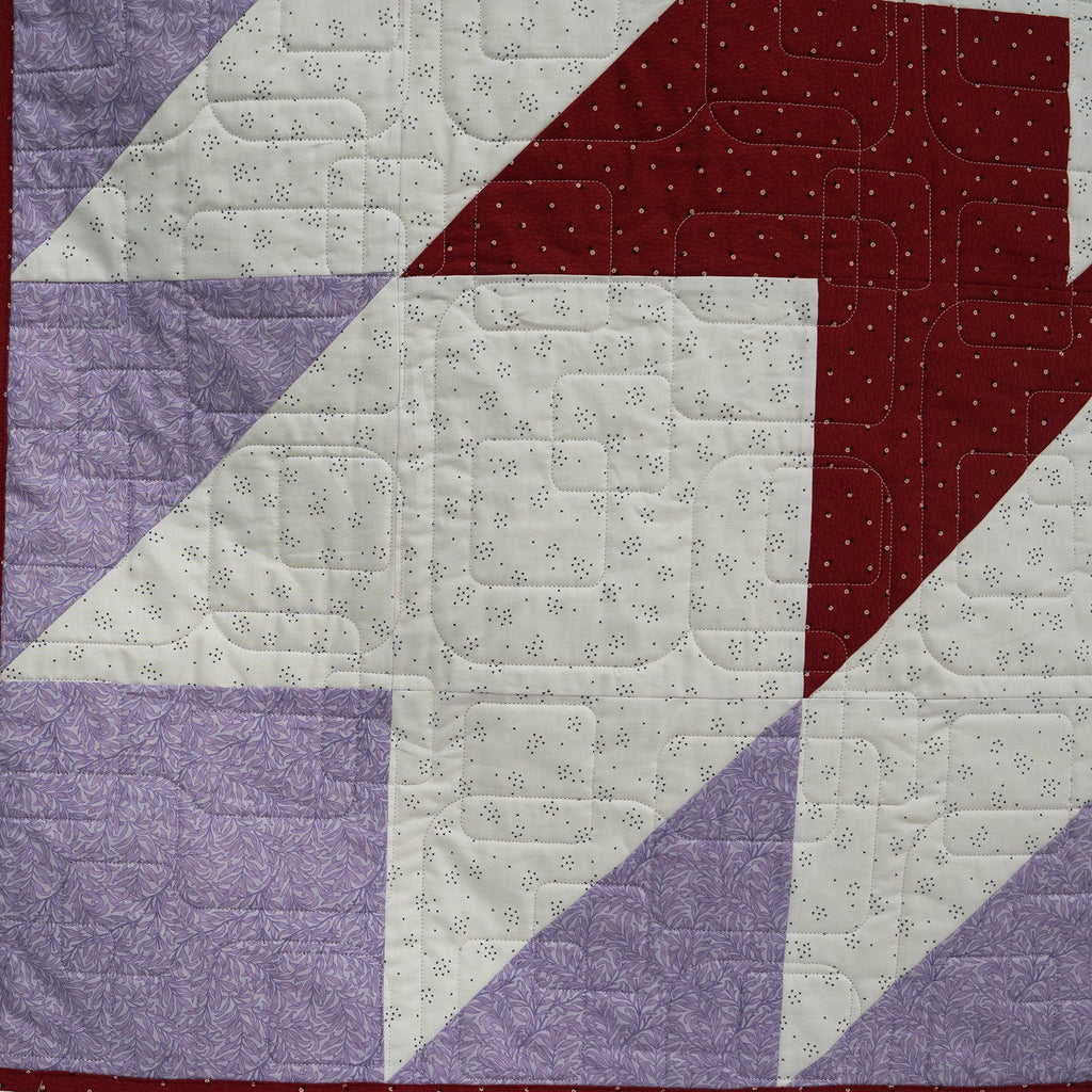 Quilt with geometric pattern featuring purple, red, and white triangles.