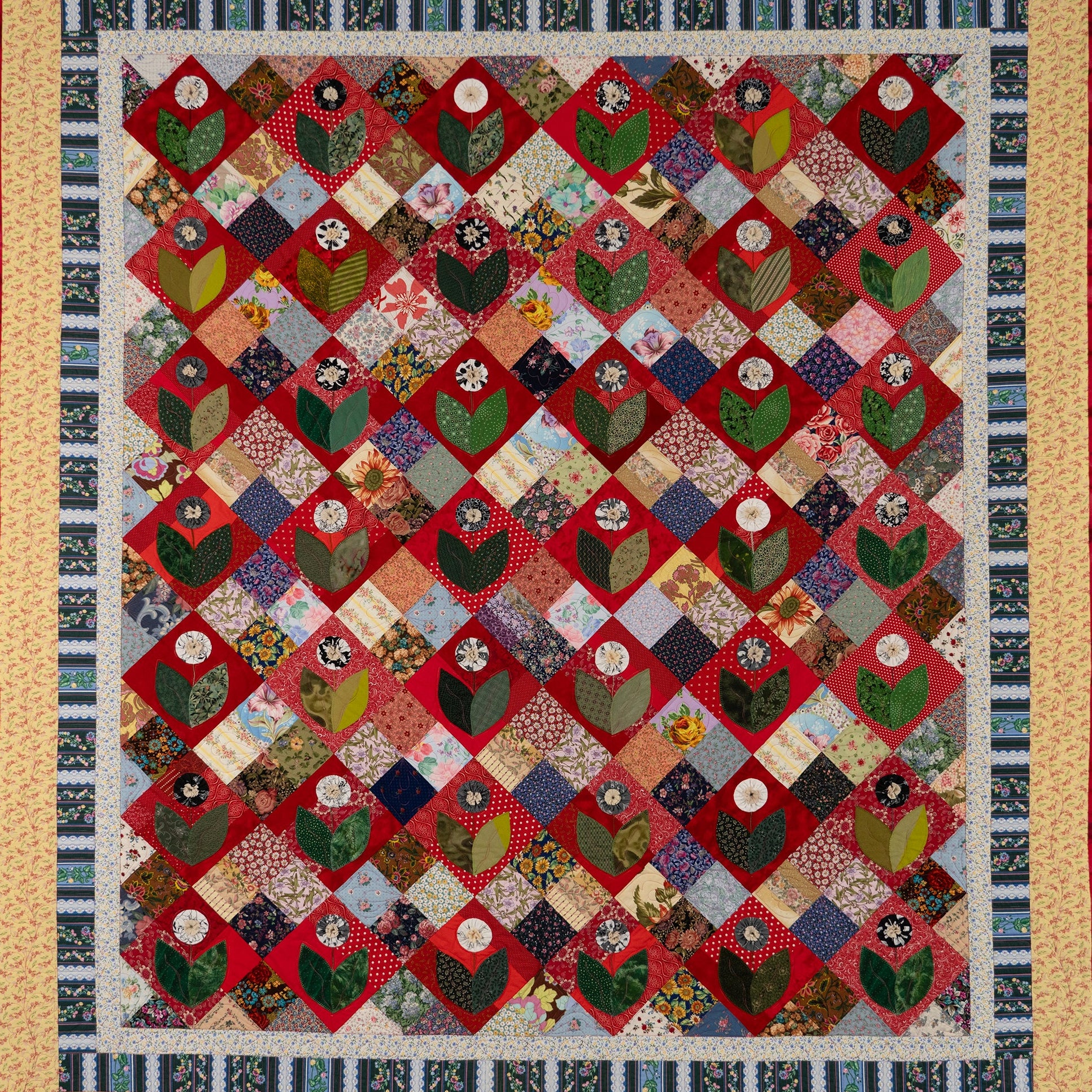 Quilt with a diamond pattern featuring a floral shape in various colors and textures.
