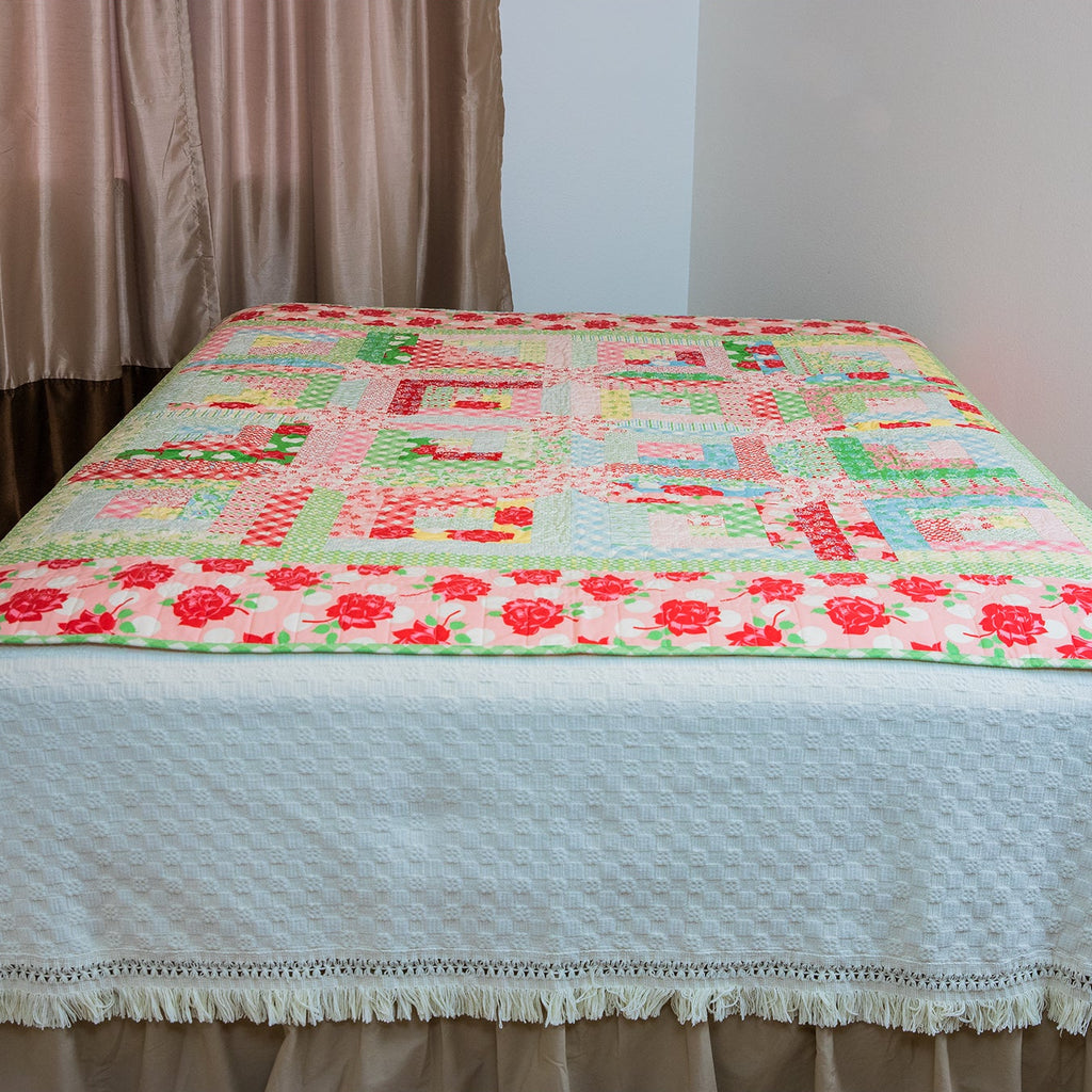 Colorful quilt on a bed with a plain wall and curtain in the background