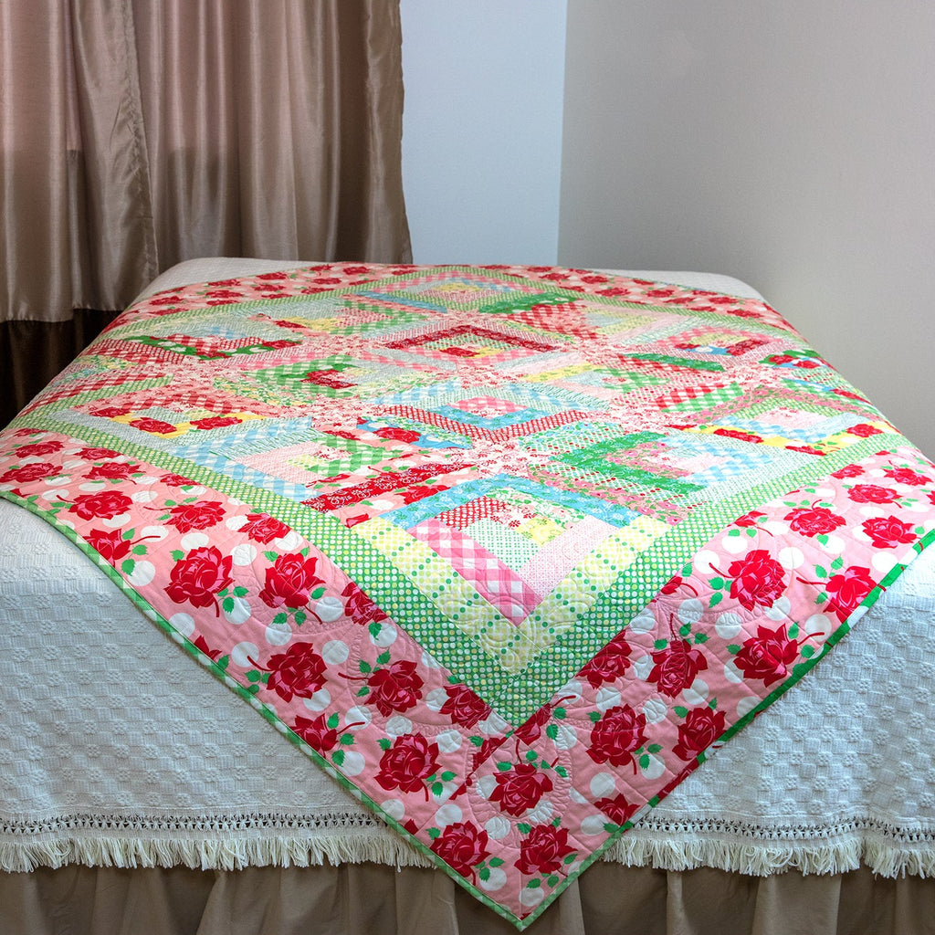 Colorful quilt with floral patterns on a bed against a plain wall.