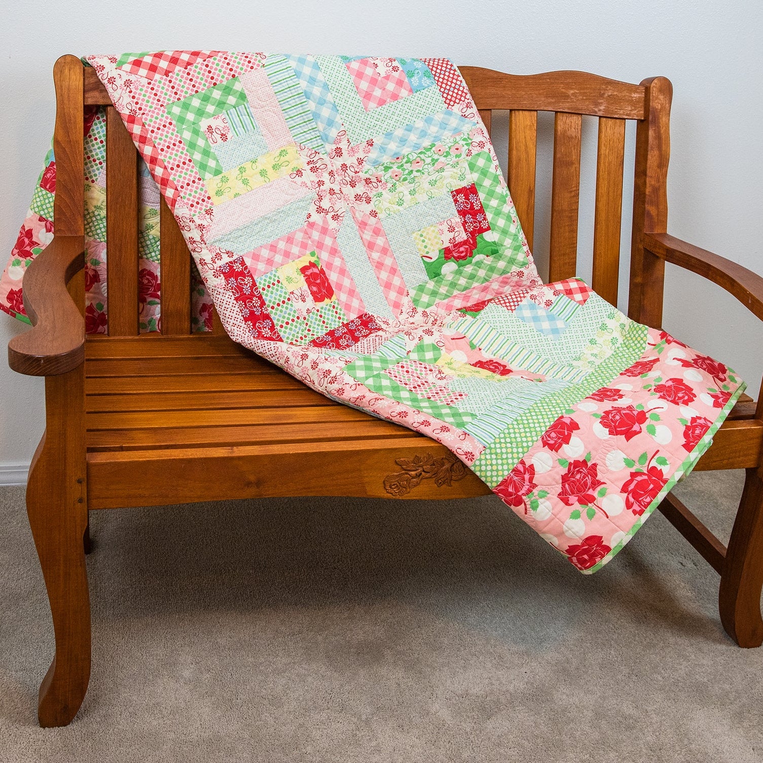 Quilt with colorful patterns draped over a wooden bench against a plain wall.