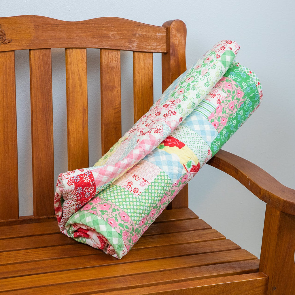 Floral quilt draped over a wooden bench against a plain wall.