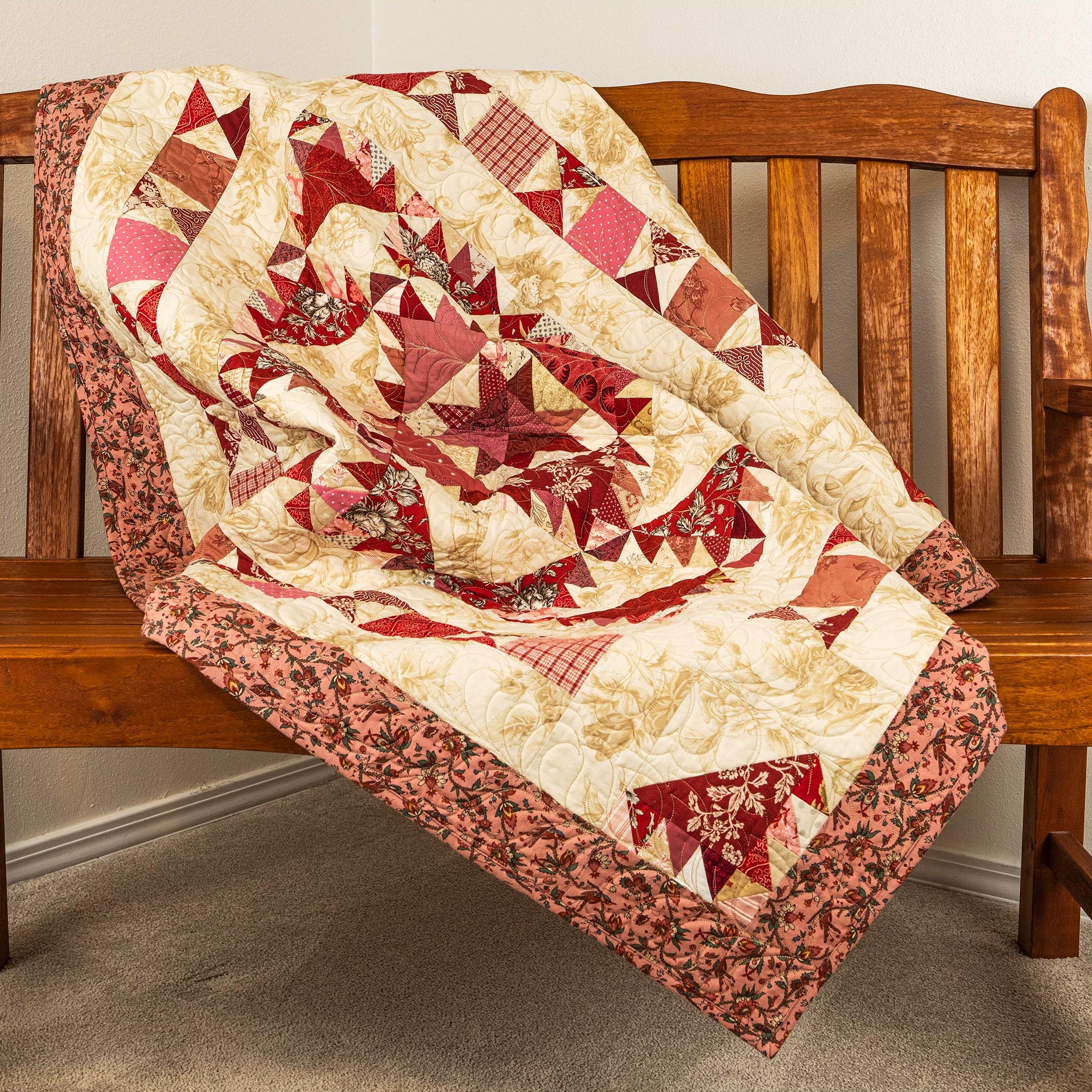Red and beige quilt displayed on a wooden bench