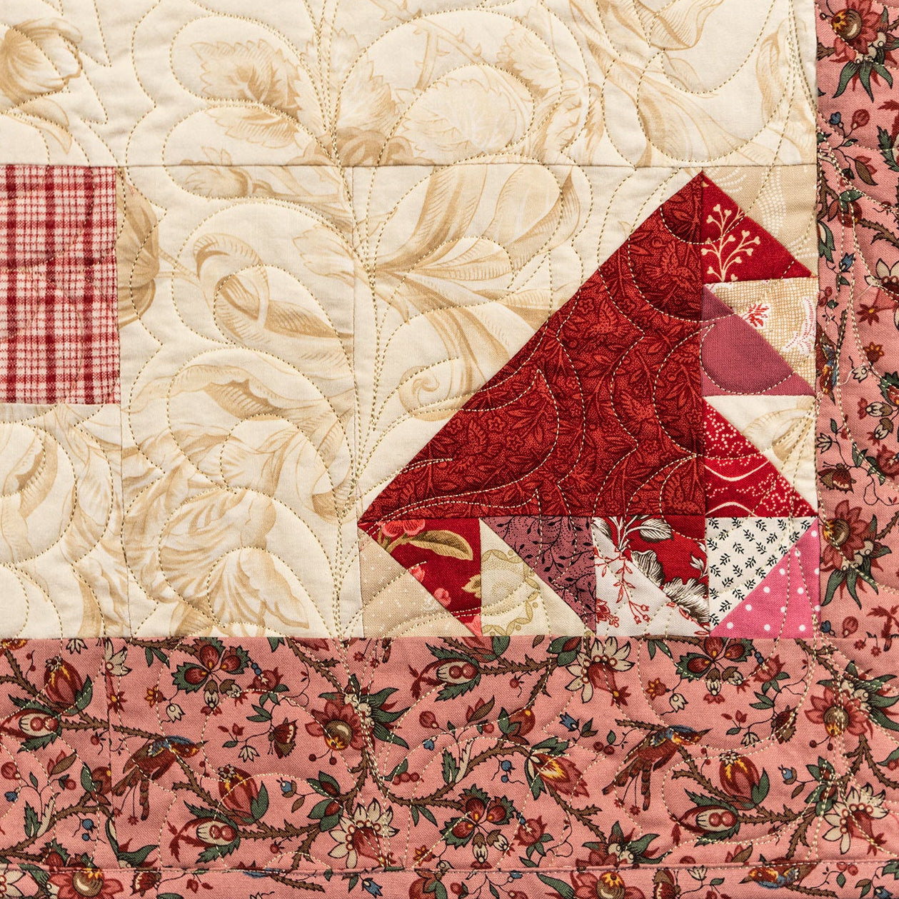 Quilt with red and beige patterned blocks on a floral border