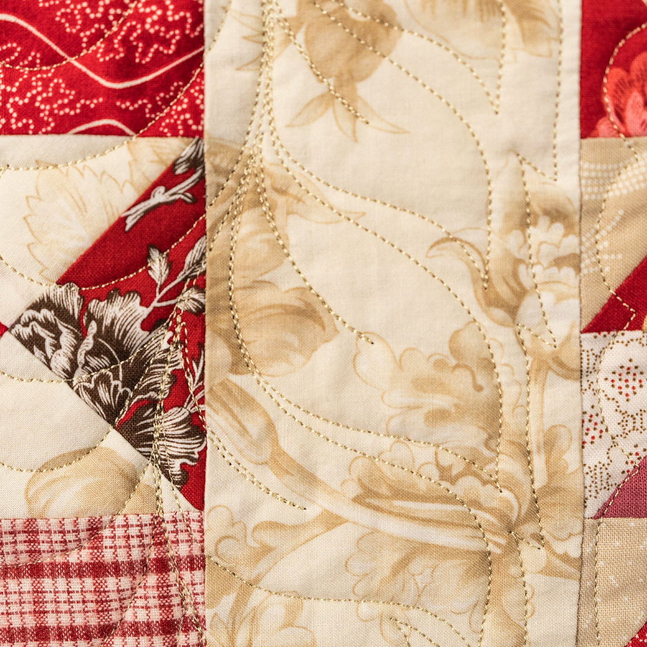 Close-up of a patchwork quilt with red, beige, and floral patterns.