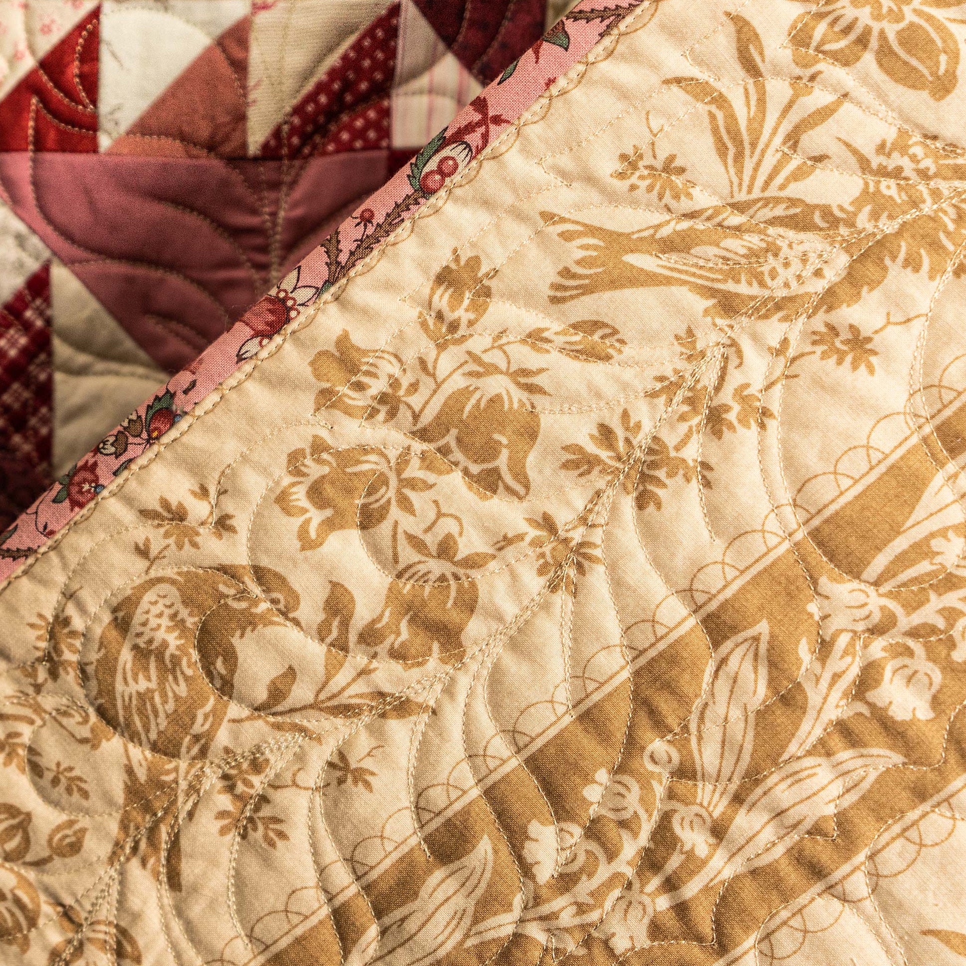 Close-up of a quilt with bird and floral patterns on beige fabric.