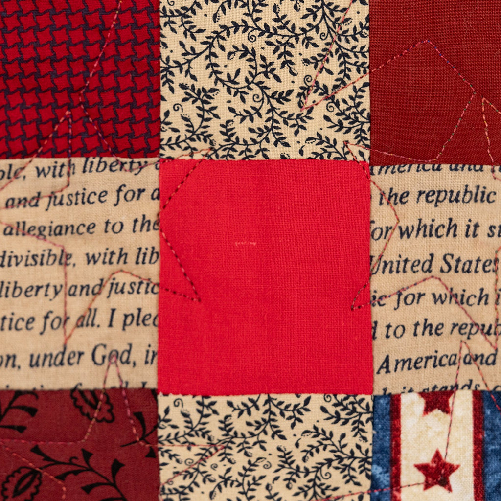 Textile patchwork with red, white, and blue patterns on a background of printed text.