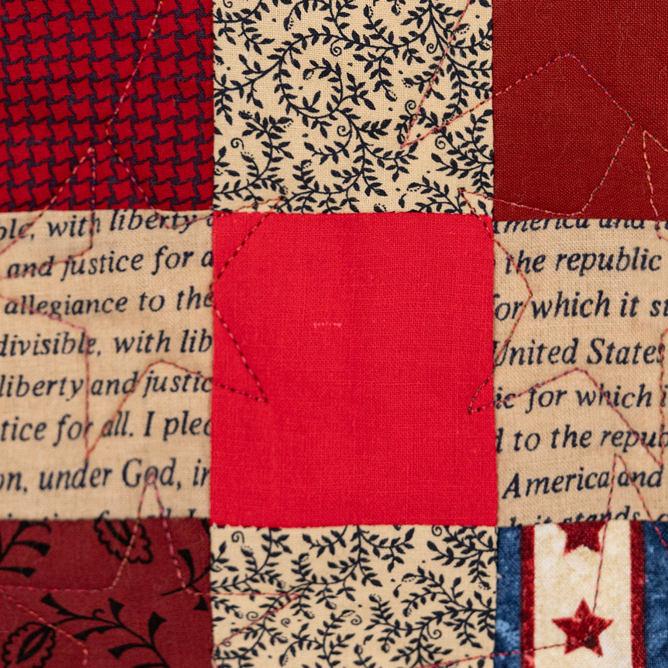 Textile patchwork with red, white, and blue patterns on a background of printed text.