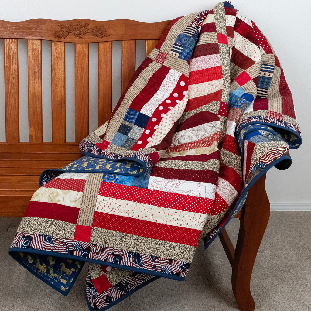 Patchwork quilt with American flag design draped over a wooden chair.