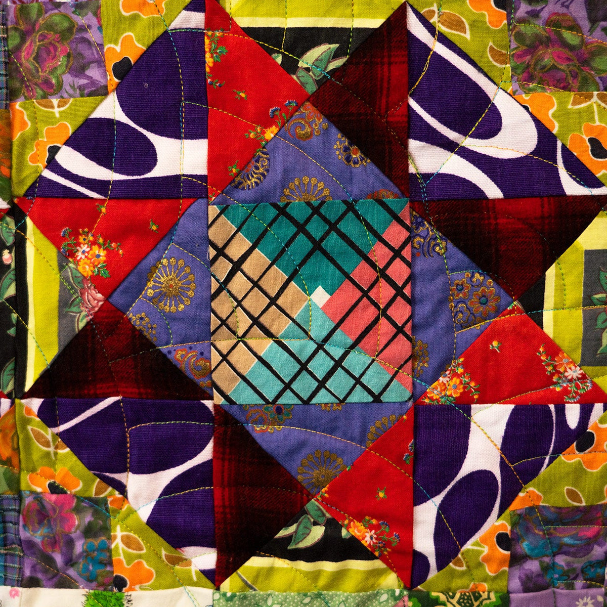 A colorful patchwork quilt featuring a central geometric star design made of various patterned fabric squares in red, purple, green, yellow, blue, and pink.
