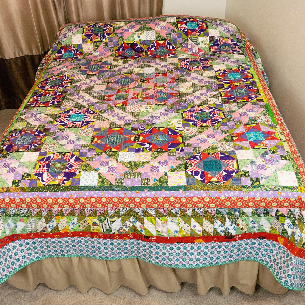 A colorful patchwork quilted bedspread with a matching ruffled bed skirt, displayed on a bed in a bedroom setting.