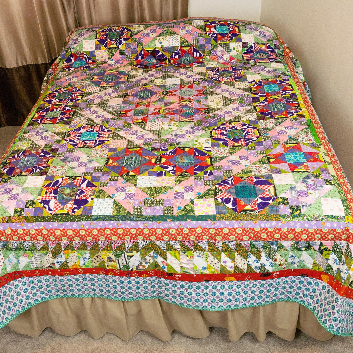 A colorful patchwork quilted bedspread with a matching ruffled bed skirt, displayed on a bed in a bedroom setting.