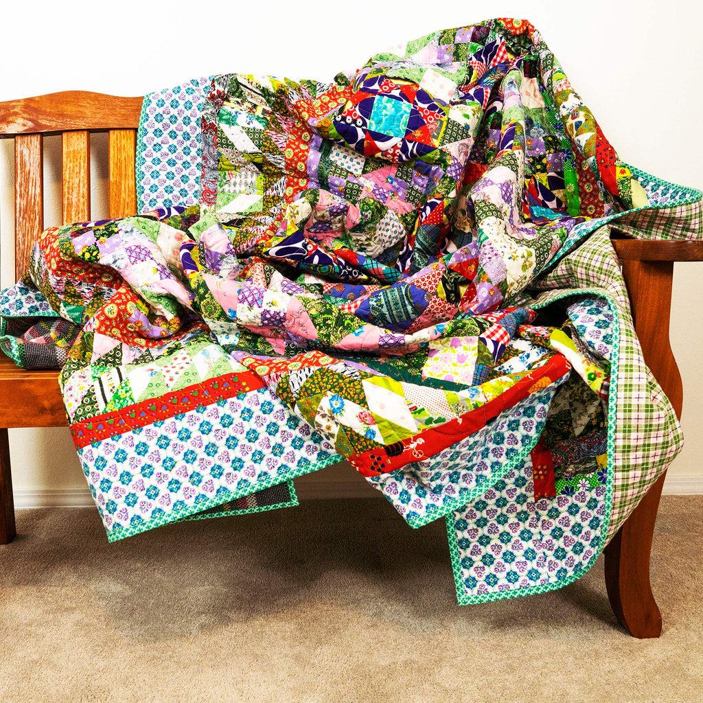 A colorful patchwork quilt draped over a wooden bench in a home setting with a beige carpet and white wall.