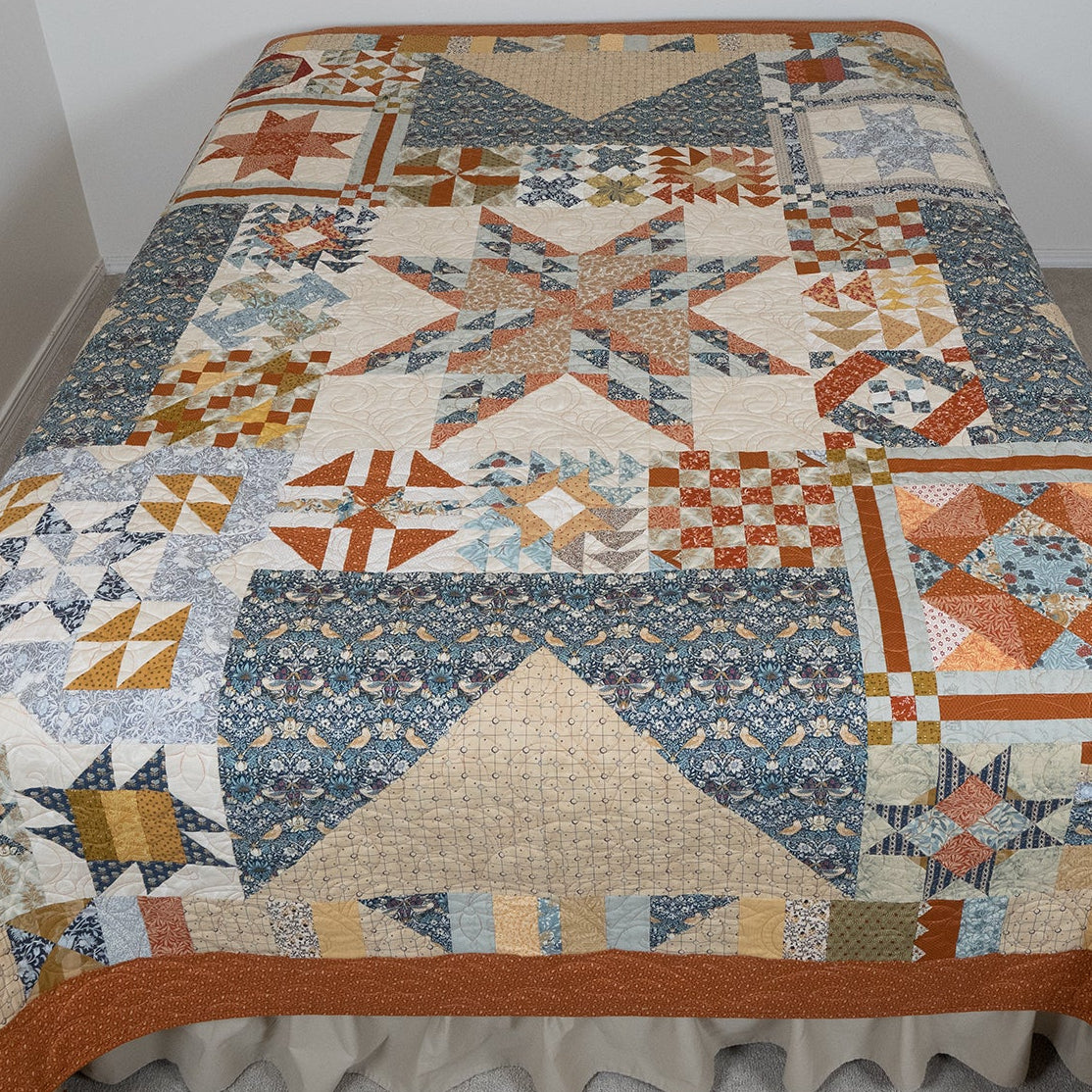 Quilt with geometric pattern on a bed against a plain wall.