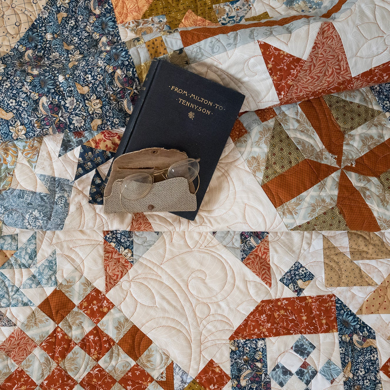 Quilt with a book and glasses on top, featuring a patchwork pattern.