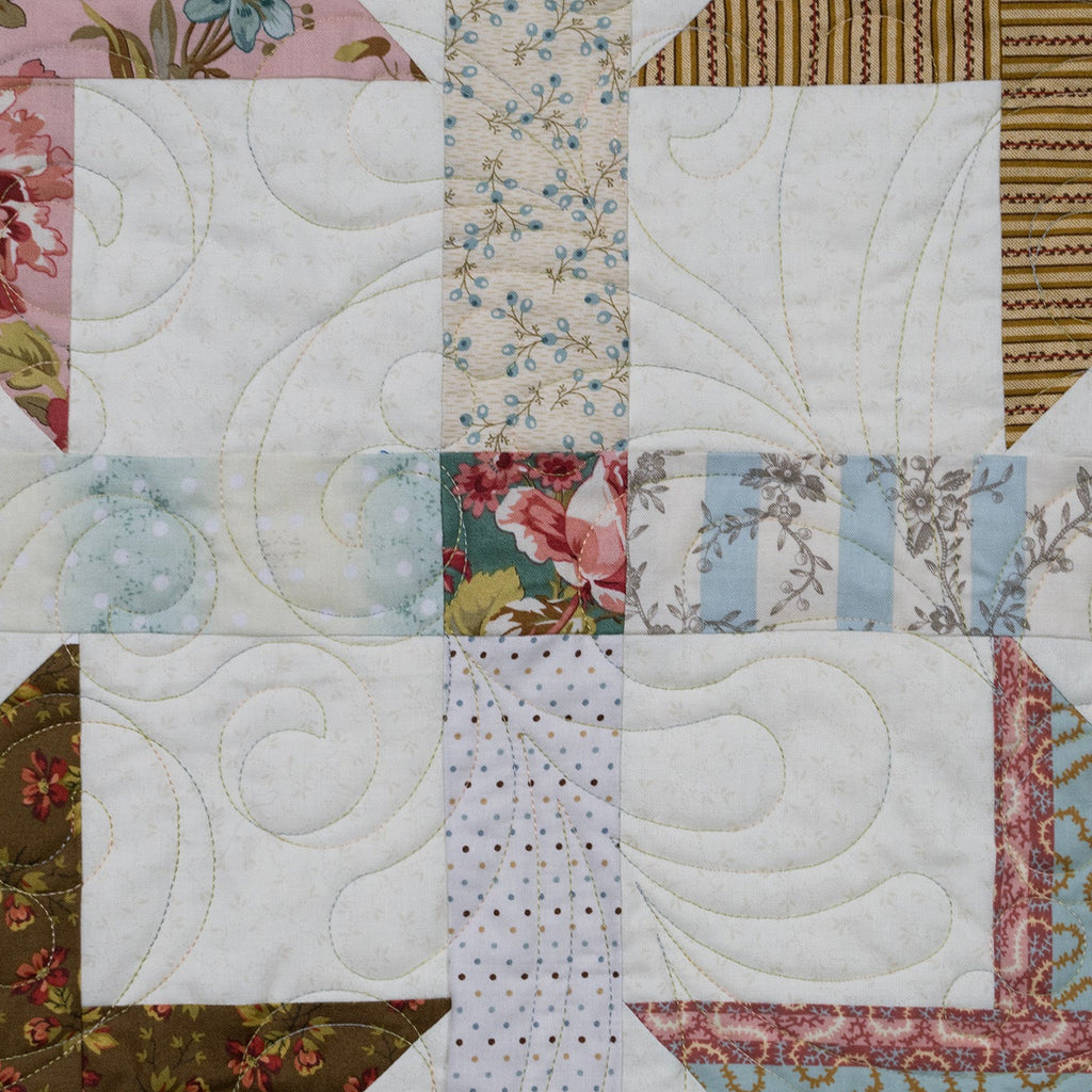 A close-up of a quilted fabric patchwork design featuring white quilted squares, floral prints, striped fabrics, and geometric patterned sections.