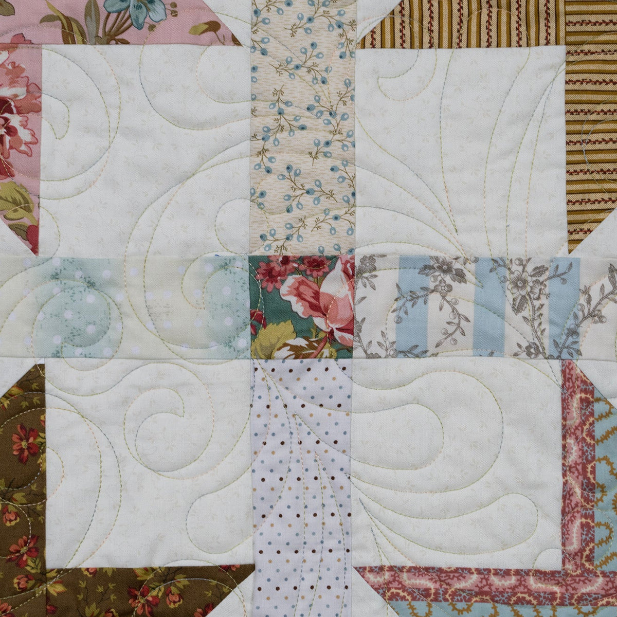 A close-up of a quilted fabric patchwork design featuring white quilted squares, floral prints, striped fabrics, and geometric patterned sections.