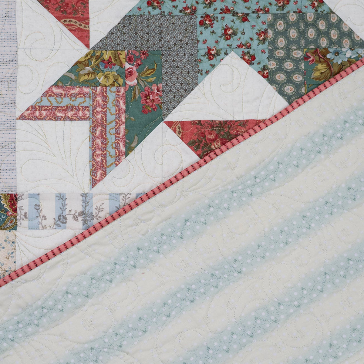 A close-up of a quilted fabric showing a diagonal split between a light blue dotted section and a multicolor patchwork section with floral and geometric patterns.