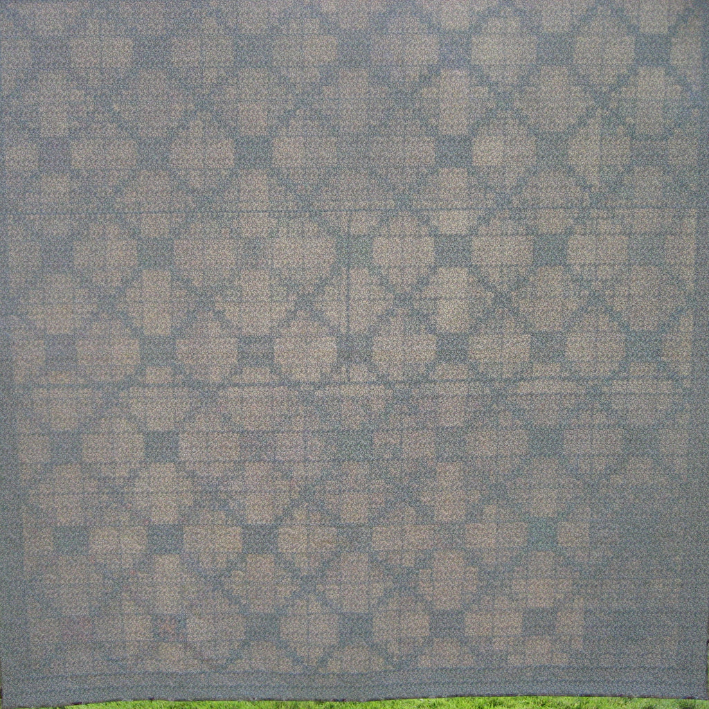 The reverse side of a quilt with a repeating geometric diamond pattern in beige and gray.