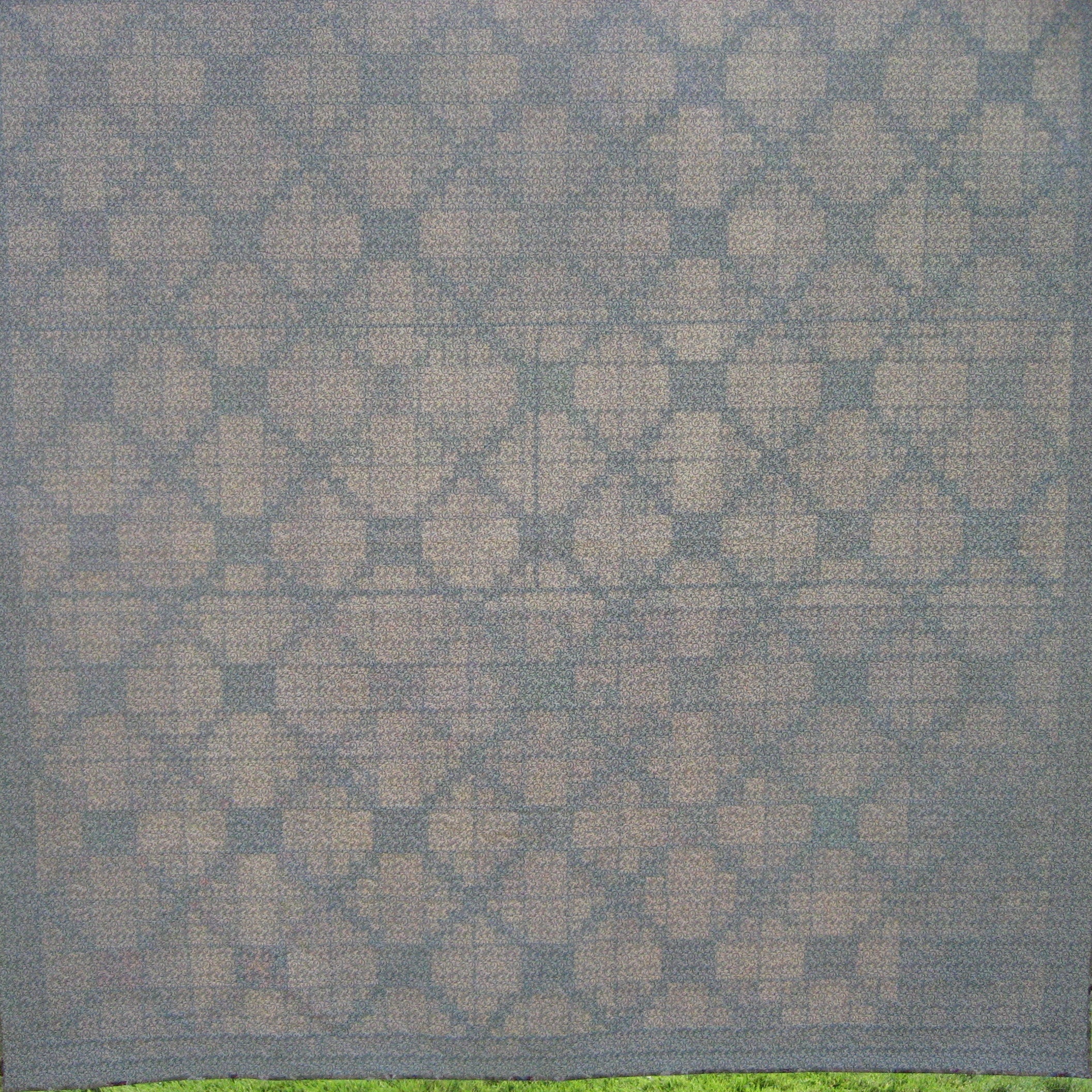 The reverse side of a quilt with a repeating geometric diamond pattern in beige and gray.
