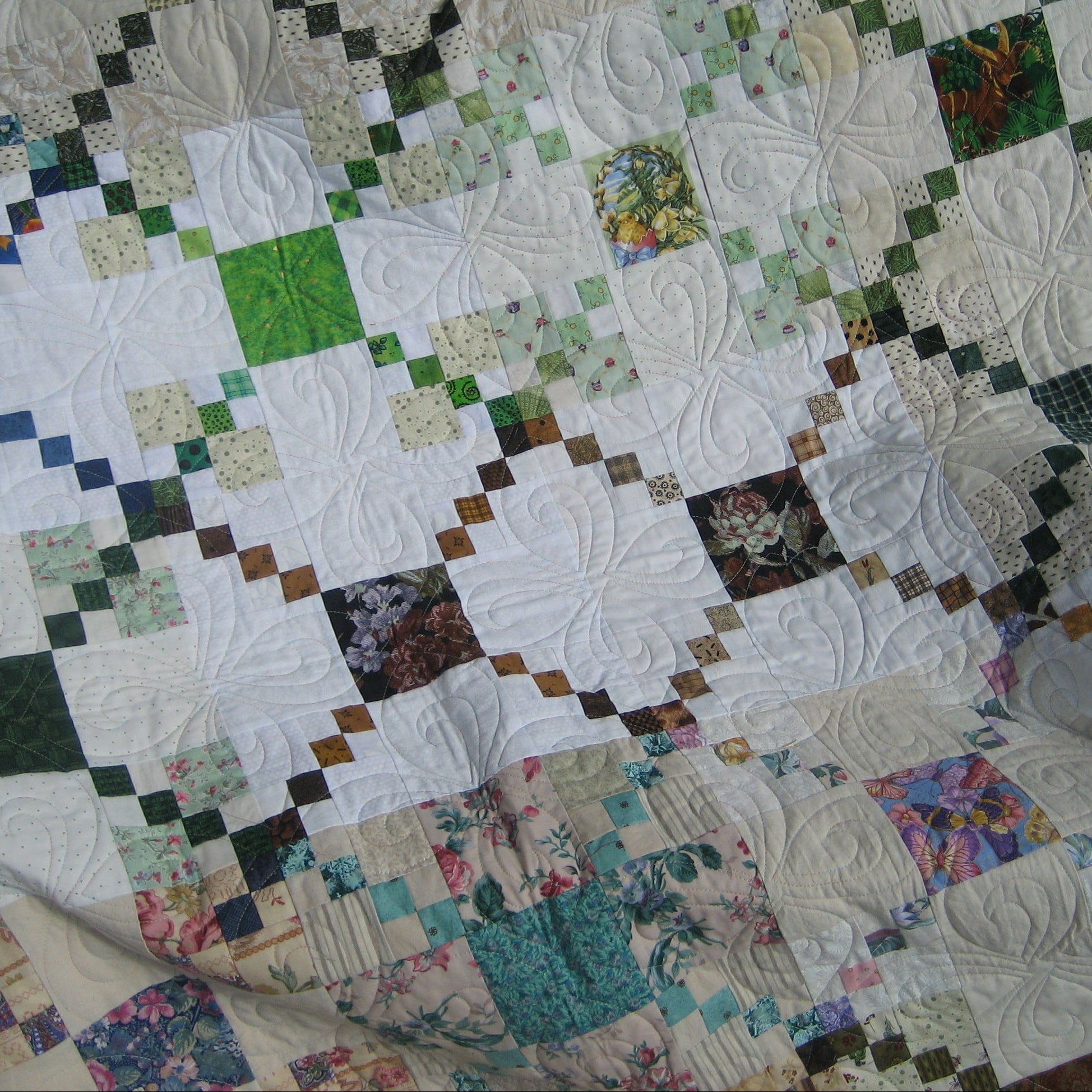 A handmade quilted patchwork blanket featuring white floral starburst blocks interspersed with small square fabric patches in green, blue, brown, and floral prints.